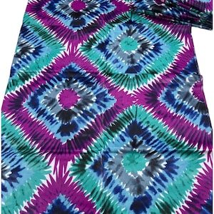 May include: A colourful textile with a repeating diamond pattern in shades of purple, teal, blue, and black. The design has a tie-dye or watercolour effect, with radiating lines emanating from the centre of each diamond. The fabric appears to be folded.