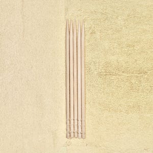 May include: A close-up of five wooden toothpicks arranged vertically on a light beige background.