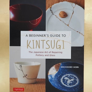 Może przedstawiać: Książka zatytułowana "A Beginner's Guide to Kintsugi: The Japanese Art of Repairing Pottery and Glass" autorstwa Michihiro Hori. Okładka przedstawia cztery obrazy ceramicznych i szklanych przedmiotów z naprawami w technice kintsugi.
