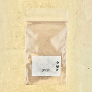 Może przedstawiać: Przezroczysty plastikowy woreczek zawierający jasnobrązowy proszek. Woreczek ma białą etykietę z tekstem "JINOKO" i "金箔" w języku japońskim.