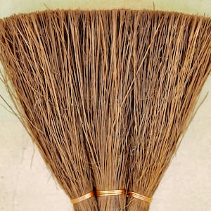 Puede incluir: Tres escobas marrones de fibra natural atadas con alambre dorado.