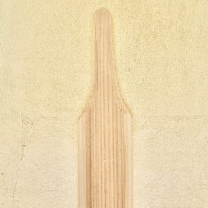 May include: A wooden paddle with a light brown color and a smooth surface. The paddle is partially submerged in a pile of white powder.