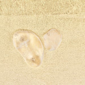 Peut inclure: Deux cristaux de quartz transparents sur un fond beige clair. Le plus grand cristal est en forme de cœur et le plus petit est de forme ovale.