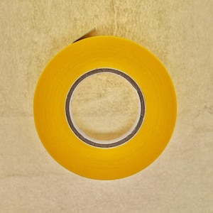 Peut inclure: Un rouleau de ruban adhésif jaune avec un noyau brun. Le ruban est sur une surface beige.