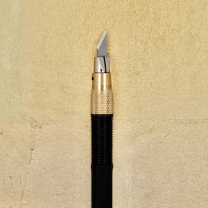 May include: A black and gold retractable craft knife with a silver blade.