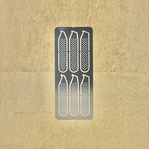 May include: A sheet of metal with six cut-out shapes, each resembling a long, thin, rectangular object with a rounded top and a dotted pattern.