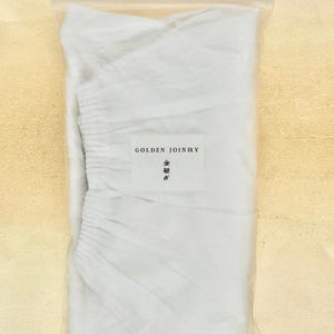 Peut inclure: Un sac en tissu blanc avec une étiquette indiquant "Golden Joinery" et un caractère japonais. Le sac est scellé dans un sac en plastique transparent.