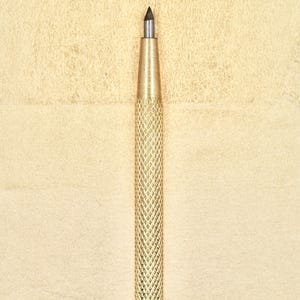 Puede incluir: Un punzón de metal dorado con una punta puntiaguda. El punzón se utiliza para perforar agujeros en cuero u otros materiales.