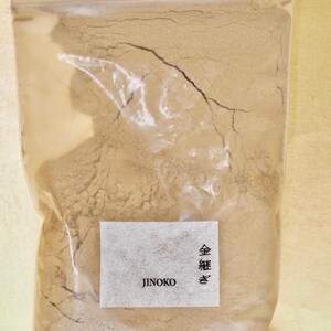 Może przedstawiać: Przezroczysty plastikowy woreczek wypełniony jasnobrązowym proszkiem. Woreczek ma białą etykietę z tekstem "JINOKO" i "金粉" w języku japońskim.