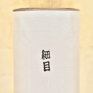 May include: A cylindrical object with a white exterior and a brown top. The Japanese characters "細目" are printed in black on the front of the cylinder. The background is a light yellow color.