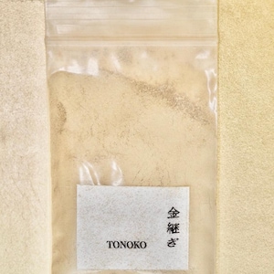 Może przedstawiać: Mały, przezroczysty woreczek plastikowy zawierający beżowy proszek. Woreczek ma białą etykietę z tekstem "TONOKO" i "金粉 き" w języku japońskim.