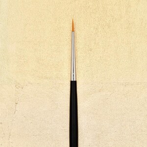 Peut inclure: Gros plan sur un petit pinceau fin à manche noir avec une pointe fine dorée.