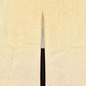Peut inclure: Un gros plan sur un petit pinceau fin avec un manche noir et une virole argentée. Le pinceau a une pointe fine et pointue.