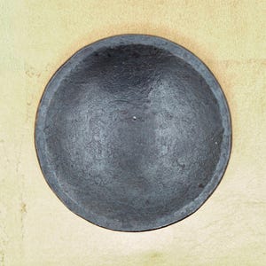 May include: A black ceramic bowl with a smooth, slightly textured surface. The bowl is round and has a slight lip around the edge.