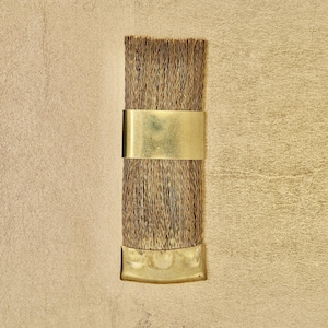 May include: A close-up of a brown paint brush with a gold metal band and a gold metal handle.