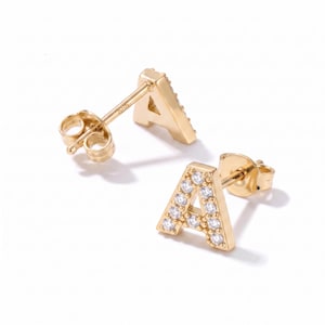 May include: A pair of gold stud earrings shaped like the letter A. Each earring features a polished gold finish and is set with small, clear, round-cut stones along the front face. The earrings include standard gold post backs for secure fastening.