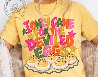 May include: A yellow short-sleeve t-shirt featuring the text I ONLY CAME FOR THE DEVILED EGGS in colorful, bold lettering. Below the text is an illustration of five deviled eggs on a scalloped-edge platter. A circular logo is in the top left.