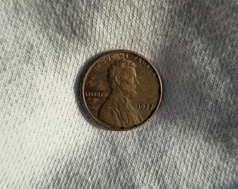 Op de afbeelding: Een koperkleurige Amerikaanse penny met de woorden "In God We Trust" en "Liberty" en het jaar "1977" erop.