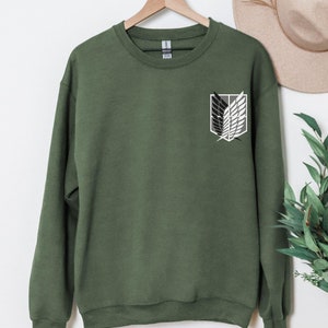 May include: A green sweatshirt with a white and black winged symbol on the left chest. The symbol is a popular anime design.