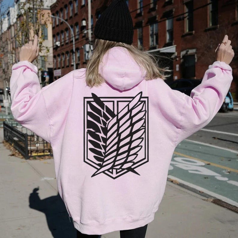 May include: A pink hoodie with a black graphic of the Attack on Titan wings of freedom symbol on the back.