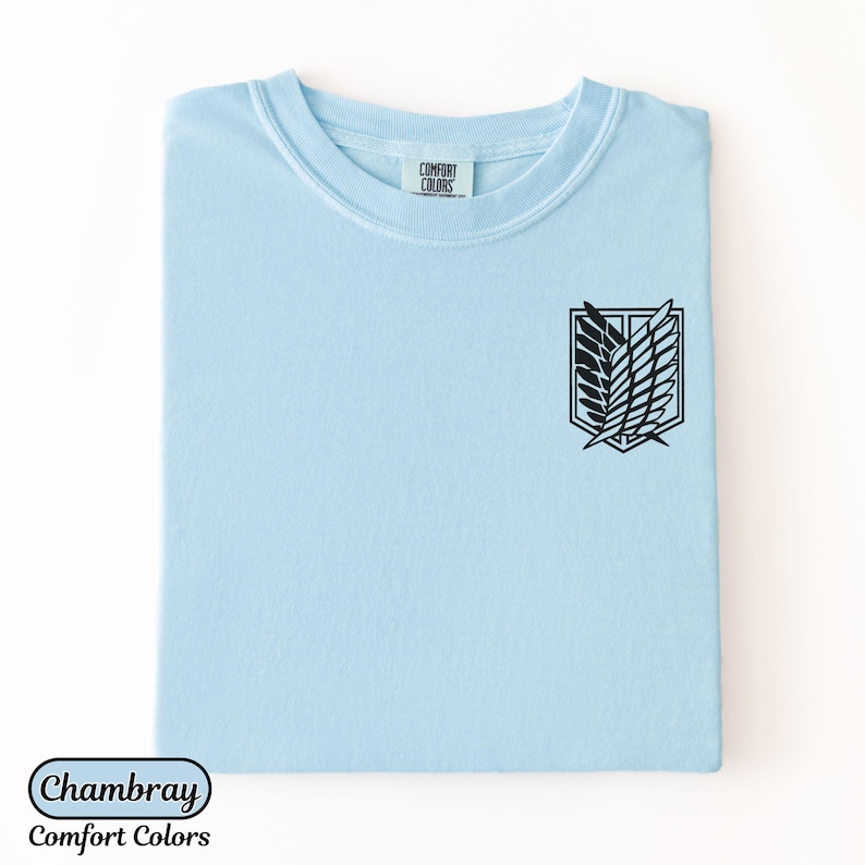 Puede incluir: Una camiseta de manga corta de color azul claro con un gr&aacute;fico negro del emblema de las Alas de la Libertad en el pecho. La etiqueta interior del cuello muestra el texto Comfort Colors. La tela es de color azul claro s&oacute;lido con cuello redondo.