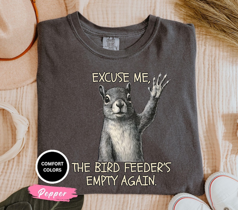 Pu&ograve; includere: T-shirt grigio scuro con grafica di uno scoiattolo che saluta, con la scritta "EXCUSE ME, THE BIRD FEEDER'S EMPTY AGAIN." La maglietta ha girocollo e maniche corte. La maglietta &egrave; di "Comfort Colors" e il colore &egrave; "Pepper".