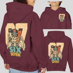 May include: Burgundy hoodie featuring a skeleton graphic wearing sunglasses and a baseball cap, with the number "67" and the words "SIX SEVEN". The design includes stars and a retro style.
