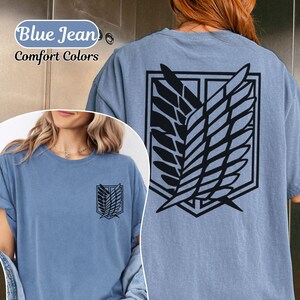 Puede incluir: Una camiseta de color azul vaquero con un gr&aacute;fico negro del emblema de las Alas de la Libertad en la espalda y una versi&oacute;n m&aacute;s peque&ntilde;a en el pecho izquierdo. El texto Blue Jean Comfort Colors es visible en la esquina superior izquierda.