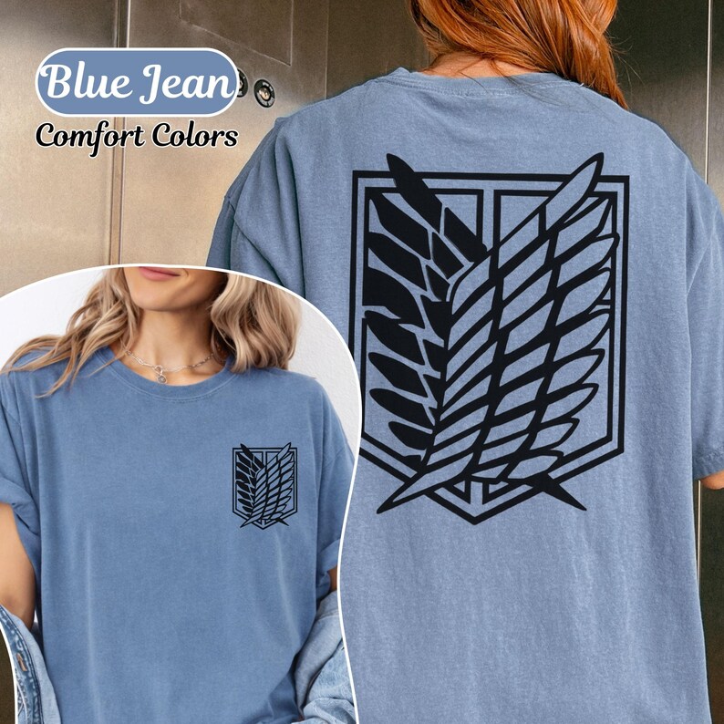Puede incluir: Una camiseta de color azul vaquero con un gr&aacute;fico negro del emblema de las Alas de la Libertad en la espalda y una versi&oacute;n m&aacute;s peque&ntilde;a en el pecho izquierdo. El texto Blue Jean Comfort Colors es visible en la esquina superior izquierda.