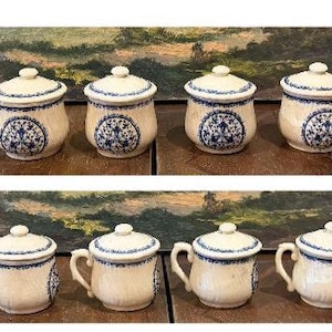 May include: Eight ceramic jars with lids, featuring a cream-colored base and intricate blue floral patterns. The jars are arranged in two rows, with four jars in each row. Some jars have handles.