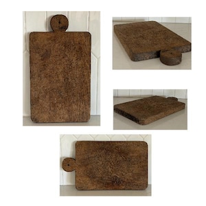 May include: A rectangular wooden cutting board with a dark brown, weathered finish and a circular handle featuring a small hole. The board displays a rough, textured surface with visible wood grain patterns, shown from multiple angles.