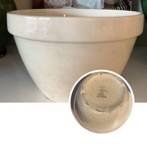 May include: Cream-colored ceramic mixing bowl with a wide rim. The bowl has a rounded shape and a smooth, glossy finish. The bottom of the bowl has a stamp that reads "C Crown Staffordshire Made in England".