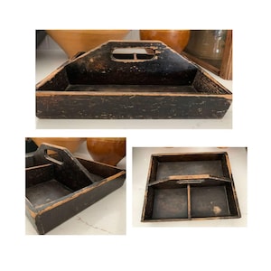 May include: A vintage, dark brown wooden tool caddy with a handle and a rectangular shape. The caddy has a distressed finish, showing signs of wear and age. The interior is divided into two compartments.