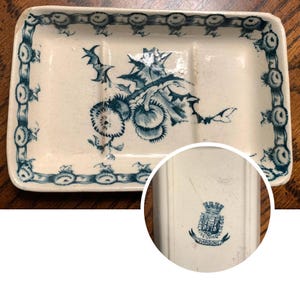 May include: Rectangular ceramic soap dish with a blue floral design and border. The dish has a raised edge and two compartments. The floral design features stylized flowers and leaves. The dish is likely vintage.
