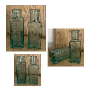 May include: Several antique, rectangular, aqua-colored glass bottles with embossed text. The bottles have a narrow neck and a square base. The image shows the bottles in different arrangements against a wooden background.