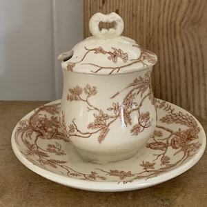 May include: A white ceramic mug with a black handle and the text "But First, Coffee" in a bold, black font. The mug is set against a blurred background, suggesting a cozy setting.