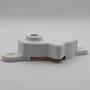 May include: White plastic 3D printed part with a rounded top and a flat base. The part has a unique shape with a cutout on the side.