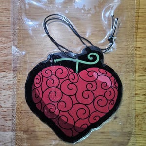 May include: A red and black heart-shaped car air freshener with a green stem and a swirl pattern. The air freshener is packaged in a clear plastic bag with a string for hanging.