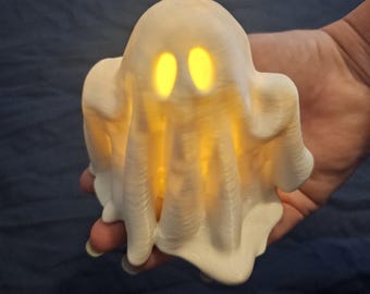 May include: A white ghost-shaped light with glowing yellow eyes. The ghost is made of a textured material and is lit from within.
