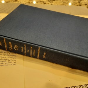 Peut inclure: Un livre reli&eacute; de couleur bleu fonc&eacute; intitul&eacute; "Cotton City: Urban Development in Antebellum Mobile, Alabama".