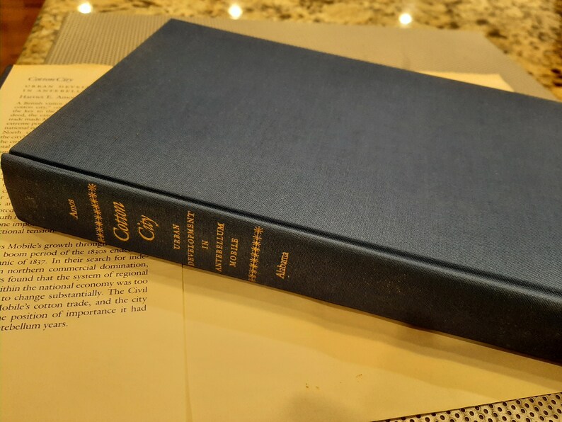 Peut inclure: Un livre reli&eacute; de couleur bleu fonc&eacute; intitul&eacute; "Cotton City: Urban Development in Antebellum Mobile, Alabama".