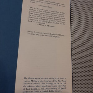 Peut inclure: Une couverture de livre avec une illustration en noir et blanc d'une ville. Le titre du livre est "Mobile: The New South City, 1815-1865" et l'auteur est Harriet E. Amos. La couverture du livre comprend &eacute;galement des citations de Leonard P. Curry et Melton A. McLaurin.