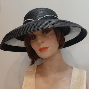 May include: A black wide-brimmed hat with a structured, ribbed texture. The hat features a black ribbon band around the crown, accented with a delicate row of small, silver-toned beads arranged in a scalloped pattern along the upper edge.