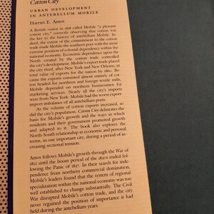 Peut inclure: Une page d'un livre intitul&eacute; "Cotton City: Urban Development in Antebellum Mobile" par Harriet E. Amos. Le texte traite de l'importance du coton pour l'&eacute;conomie de la ville et de sa d&eacute;pendance envers le Nord pour le commerce.
