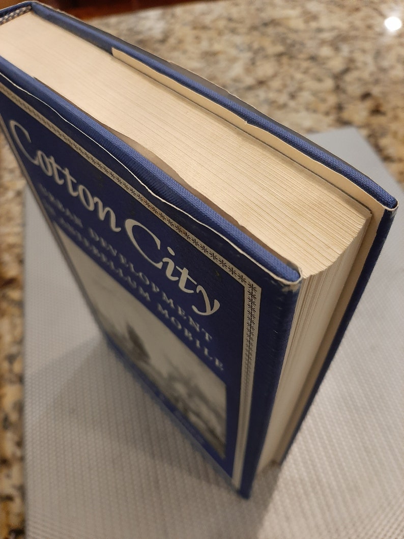 Peut inclure: Un livre reli&eacute; de couleur bleue avec le titre "Cotton City" et le texte "Urban Development in Mobile" sur le dos.