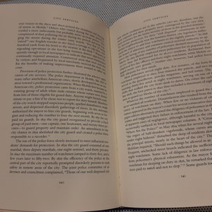 Peut inclure: Deux livres ouverts avec des pages montrant du texte sur les services municipaux dans les ann&eacute;es 1800. Le texte traite de l'&eacute;volution des forces de police &agrave; Mobile, en Alabama, d'un syst&egrave;me bas&eacute; sur le volontariat &agrave; une force plus professionnelle et r&eacute;mun&eacute;r&eacute;e. Les livres sont reli&eacute;s en cuir brun avec des accents dor&eacute;s.