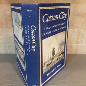Peut inclure: Un livre bleu intitul&eacute; "Cotton City: Urban Development in Antebellum Mobile" par Harriet E. Amos. La couverture du livre pr&eacute;sente une photographie en noir et blanc d'un port avec des navires.