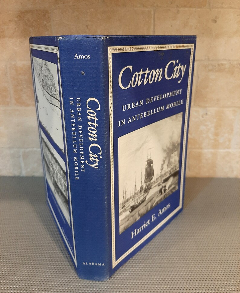 Peut inclure: Un livre bleu intitul&eacute; "Cotton City: Urban Development in Antebellum Mobile" par Harriet E. Amos. La couverture du livre pr&eacute;sente une photographie en noir et blanc d'un port avec des navires.
