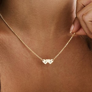 May include: A gold chain necklace with two small heart pendants. The hearts are engraved with the letters "L" and "S".