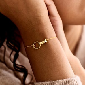 Könnte beinhalten: Ein goldfarbenes Kettenarmband mit einem kreisförmigen Glied, das mit einem kleinen rechteckigen Stab verbunden ist, in den der Name Grace eingraviert ist. Die feine Kette wird mit einem Verschluss gesichert und bildet ein minimalistisches Schmuckstück.